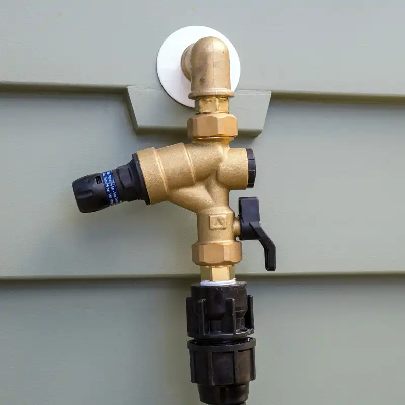 Brass backflow prevention device installed on an exterior wall for safe water supply protection