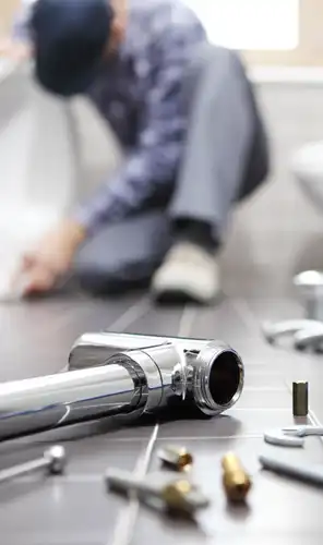 Plumber installing bathroom pipework Plumbing parts on a bathroom floor with a plumber working in the background
